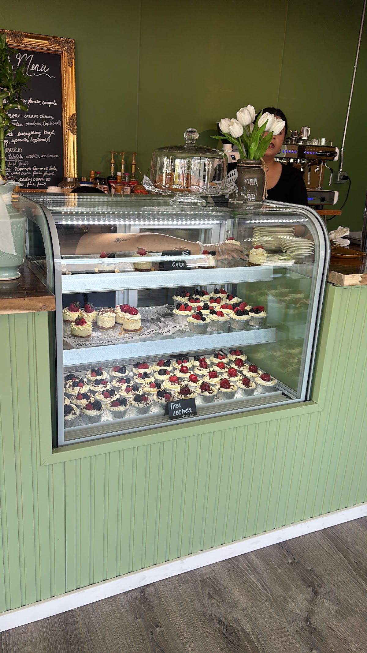 The pastry case at Hortencia, with tres leches cups, fresh tulips and a gold-framed chalkboard menu